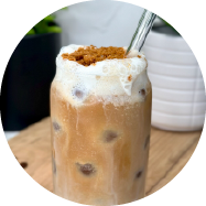 A tall cylinder glass filled with a mocha coffee and sphere ice cubes, topped with white cold foam and brown Biscoff cookie crumbs.