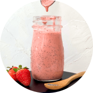 A glass bottle filled with a creamy pink dressing speckled with black little poppyseeds. A spoon is hovering over top with a drip of the dressing dripping off of it back into the jar.