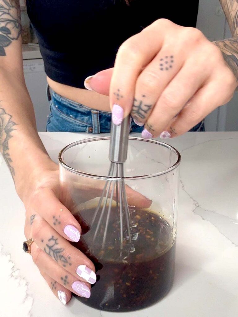 Glass jar and whisk filled with sesame and ginger sauce